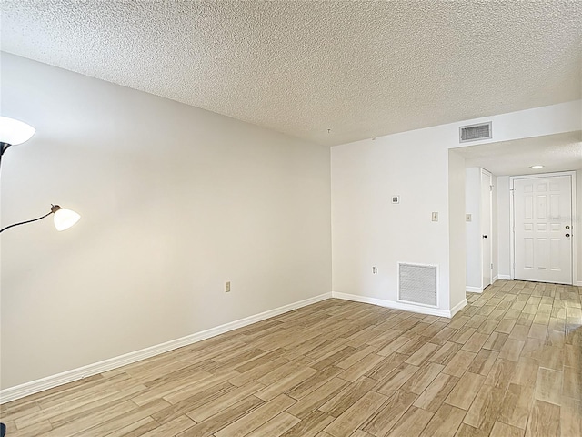 spare room with light wood-style flooring, a textured ceiling, and baseboards