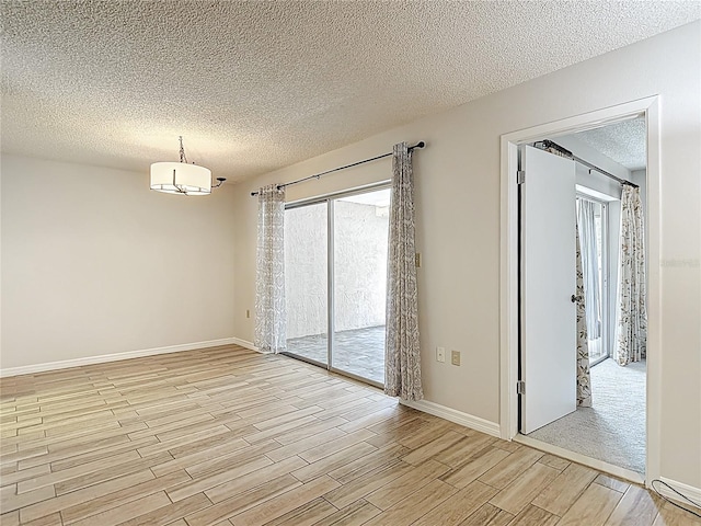 empty room with light wood-style floors, a textured ceiling, and baseboards