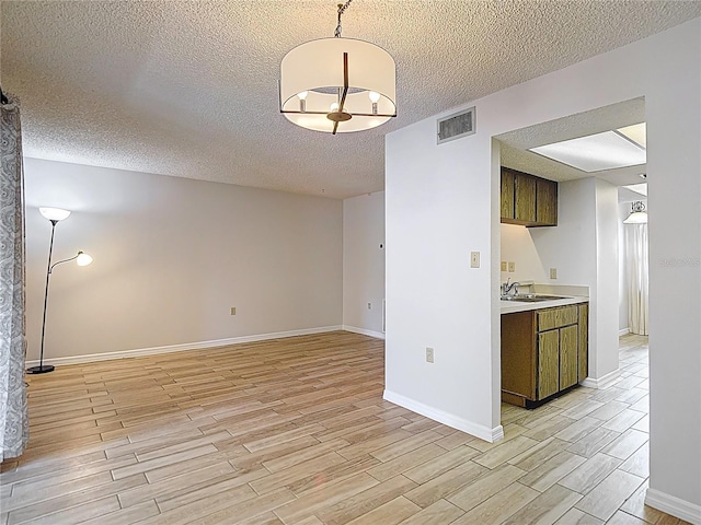kitchen with light wood-style floors, light countertops, a textured ceiling, baseboards, and dark brown cabinetry