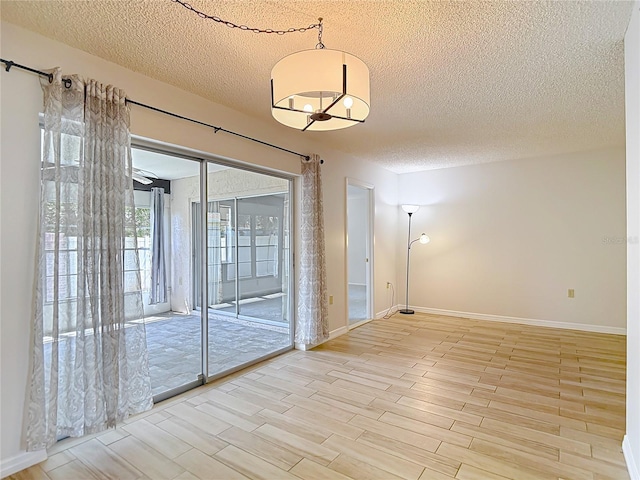 spare room with a textured ceiling, light wood-type flooring, and baseboards