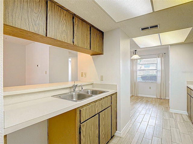 kitchen featuring a sink, light countertops, baseboards, and a textured ceiling