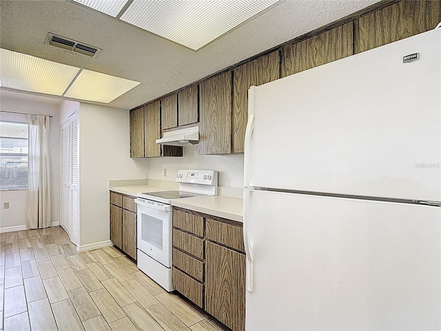 kitchen with white appliances, under cabinet range hood, light countertops, baseboards, and light wood finished floors