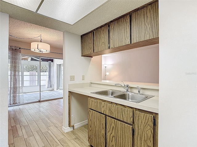 kitchen with a sink, a textured ceiling, light countertops, and light wood-type flooring