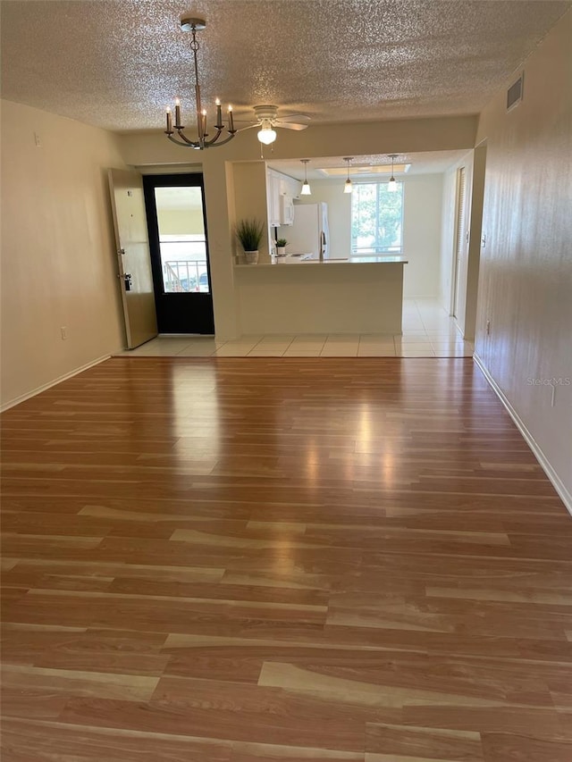 210 Cypress Ct Unit 122, Oldsmar, FL 34677 - unfurnished living room featuring light wood-type flooring, a textured ceiling, a chandelier, healthy amount of natural light, and baseboards