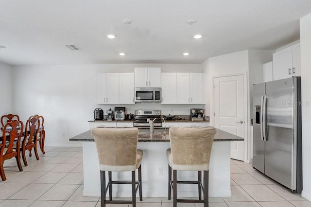 kitchen with appliances with stainless steel finishes, an island with sink, a breakfast bar, recessed lighting, and dark stone counters