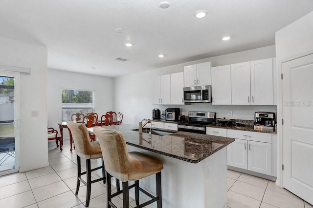 kitchen with stainless steel appliances, a sink, a kitchen bar, a center island with sink, and light tile patterned floors