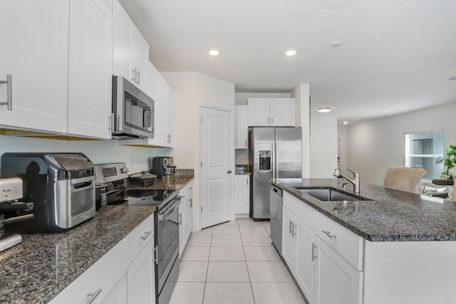 kitchen featuring appliances with stainless steel finishes, a sink, light tile patterned floors, an island with sink, and white cabinetry