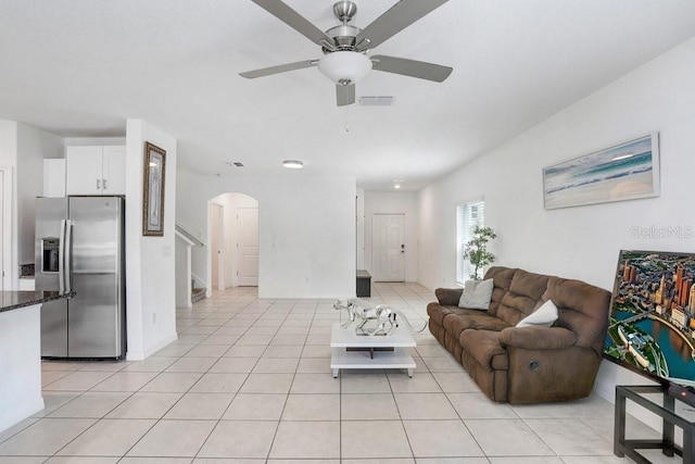 living room with arched walkways, ceiling fan, stairway, light tile patterned floors, and baseboards