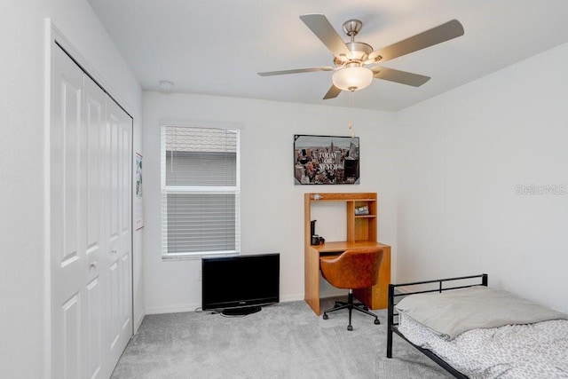 bedroom featuring a closet, light colored carpet, ceiling fan, baseboards, and a desk