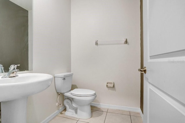 bathroom with toilet, tile patterned floors, baseboards, and a sink