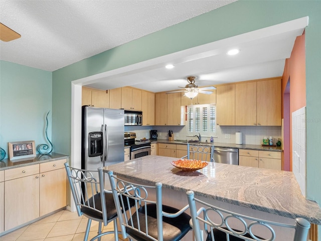 4700 Cove Cir Unit 301, Saint Petersburg, FL 33708 - kitchen with appliances with stainless steel finishes, light brown cabinets, a breakfast bar area, a ceiling fan, and recessed lighting