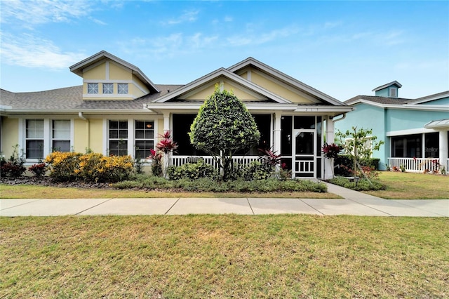 view of front of house with a front yard, stucco siding, a shingled roof, and a sunroom