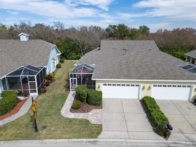 view of front of home featuring a shingled roof, driveway, a front yard, an attached garage, and glass enclosure
