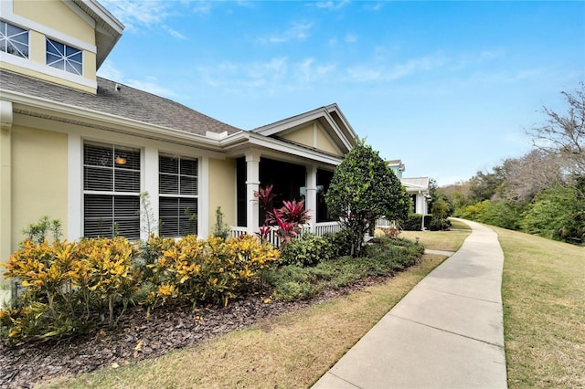 view of home's exterior with a shingled roof, stucco siding, a yard, and a porch