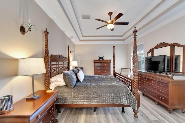 bedroom featuring a raised ceiling, light wood-style flooring, and ornamental molding
