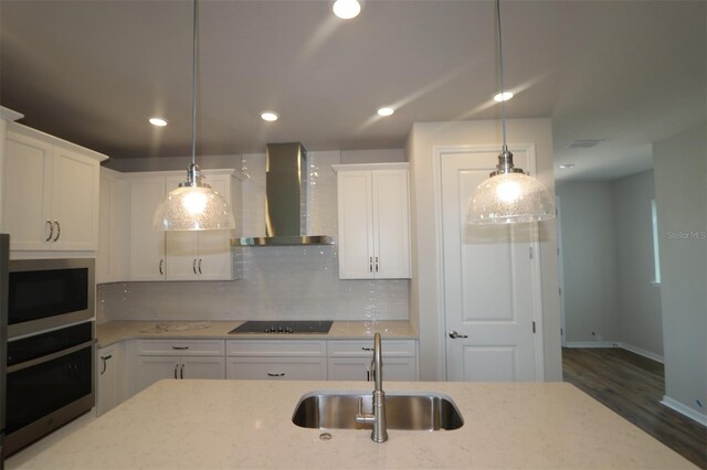 kitchen featuring oven, wall chimney exhaust hood, a sink, built in microwave, and white cabinetry