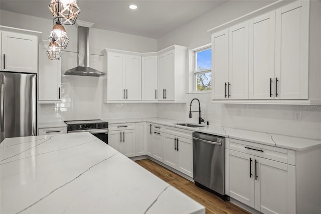 kitchen with appliances with stainless steel finishes, wall chimney range hood, a sink, tasteful backsplash, and white cabinetry