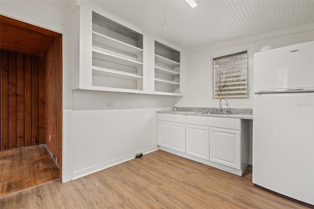 916 E Broad St, Tampa, FL 33604 - kitchen with freestanding refrigerator, a sink, light wood finished floors, white cabinets, and wood walls