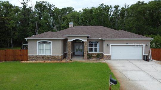 ranch-style home featuring stone siding, stucco siding, a garage, driveway, and a chimney