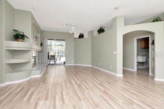 unfurnished living room with light wood-type flooring, a fireplace with raised hearth, baseboards, arched walkways, and a ceiling fan
