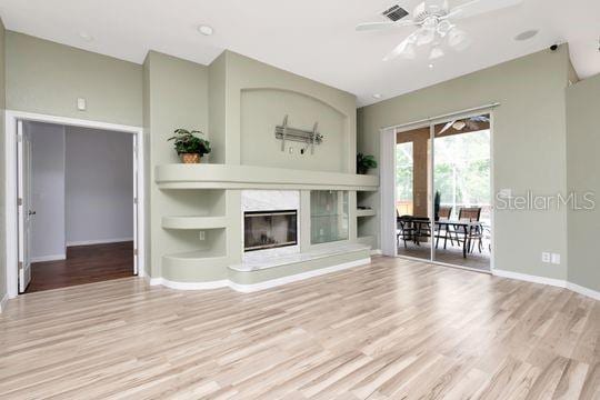living area with wood finished floors, a ceiling fan, a tiled fireplace, and baseboards