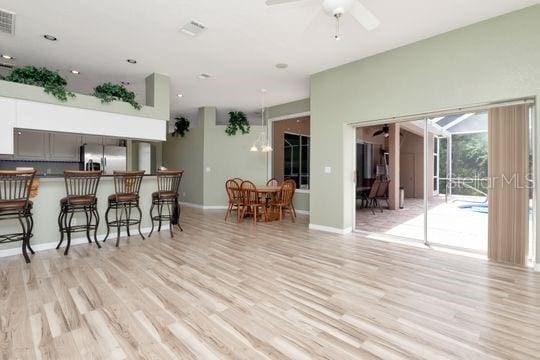 kitchen featuring stainless steel fridge with ice dispenser, a kitchen breakfast bar, light wood-style floors, a ceiling fan, and baseboards