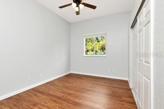 unfurnished bedroom featuring baseboards, wood finished floors, a closet, and ceiling fan
