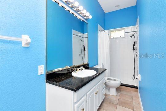full bath with toilet, a shower with shower curtain, a textured wall, vanity, and tile patterned floors