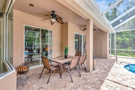 view of patio featuring ceiling fan, glass enclosure, and outdoor dining area