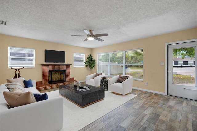 living room with wood finished floors, a textured ceiling, ceiling fan, a brick fireplace, and baseboards