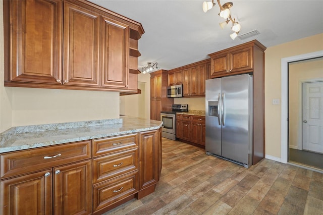 kitchen with appliances with stainless steel finishes, brown cabinets, open shelves, wood finished floors, and light stone countertops