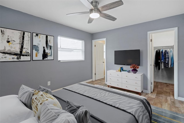 bedroom featuring a spacious closet, light wood-type flooring, a closet, baseboards, and a ceiling fan