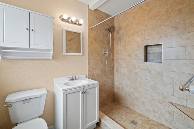 bathroom with toilet, tiled shower, and vanity
