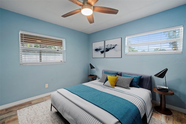 bedroom featuring multiple windows, baseboards, a ceiling fan, and wood finished floors