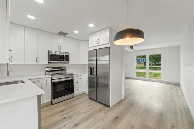 7400 Belvedere Ter, New Port Richey, FL 34655 - kitchen featuring appliances with stainless steel finishes, light wood-type flooring, light countertops, a sink, and white cabinetry