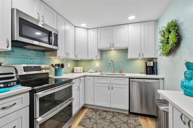 10216 Regal Dr Unit 310, Largo, FL 33774 - kitchen featuring appliances with stainless steel finishes, a sink, light wood finished floors, white cabinetry, and backsplash