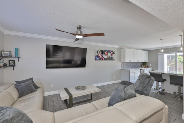 living area featuring wood finished floors, baseboards, crown molding, a ceiling fan, and a textured ceiling