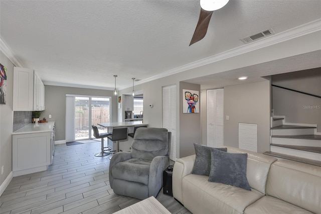 living area featuring ornamental molding, ceiling fan, stairway, a textured ceiling, and baseboards