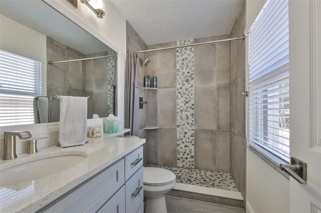 bathroom with a tile shower, vanity, toilet, wood finished floors, and a textured ceiling