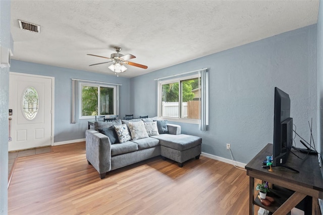living room featuring light wood-style floors, healthy amount of natural light, ceiling fan, baseboards, and a textured ceiling