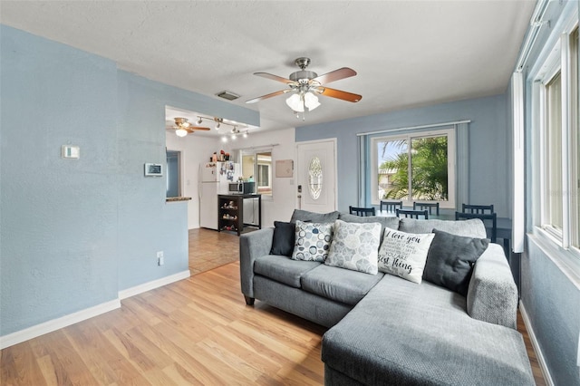 living area featuring ceiling fan, a textured wall, wood finished floors, and baseboards