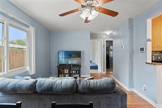 living area with light wood-style flooring, ceiling fan, and baseboards