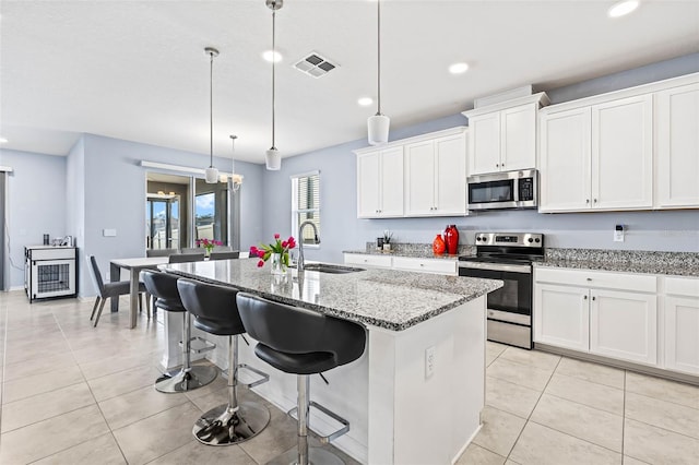 3071 Marine Grass Dr, Wimauma, FL 33598 - kitchen featuring stainless steel appliances, a sink, a kitchen island with sink, light tile patterned floors, and light stone countertops