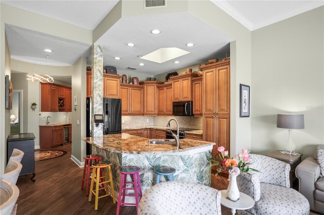 205 Brightwater Dr Unit 101, Clearwater Beach, FL 33767 - kitchen featuring black appliances, light stone counters, a kitchen bar, brown cabinets, and dark wood-type flooring
