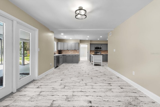 kitchen with gray cabinetry, stainless steel microwave, dishwasher, light wood finished floors, and decorative backsplash