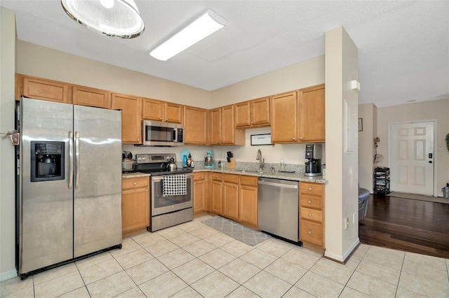 kitchen featuring stainless steel appliances, a sink, light tile patterned flooring, and light stone countertops
