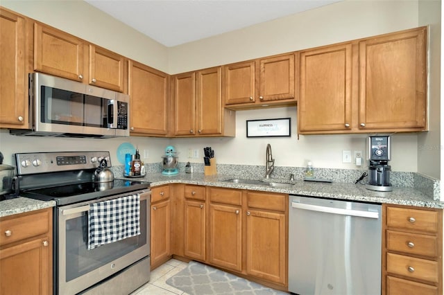 kitchen featuring stainless steel appliances, a sink, light stone countertops, and light tile patterned floors