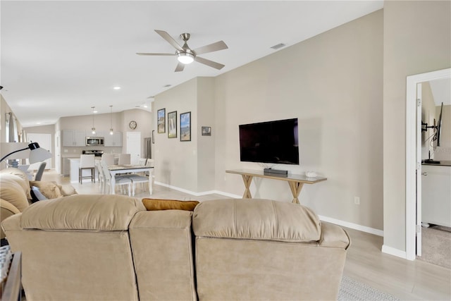 living area with a ceiling fan, vaulted ceiling, baseboards, and light wood-style flooring