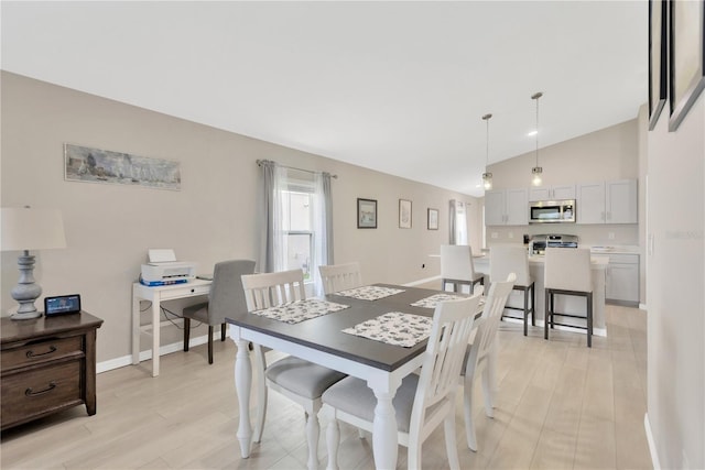 dining area with light wood-style flooring, vaulted ceiling, and baseboards