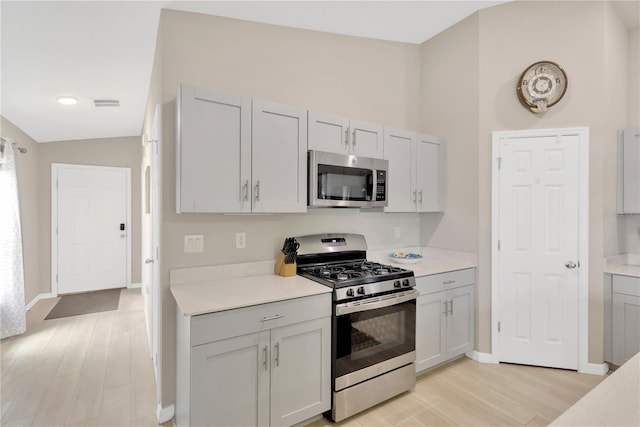 kitchen featuring stainless steel appliances, light wood-style flooring, light countertops, baseboards, and lofted ceiling
